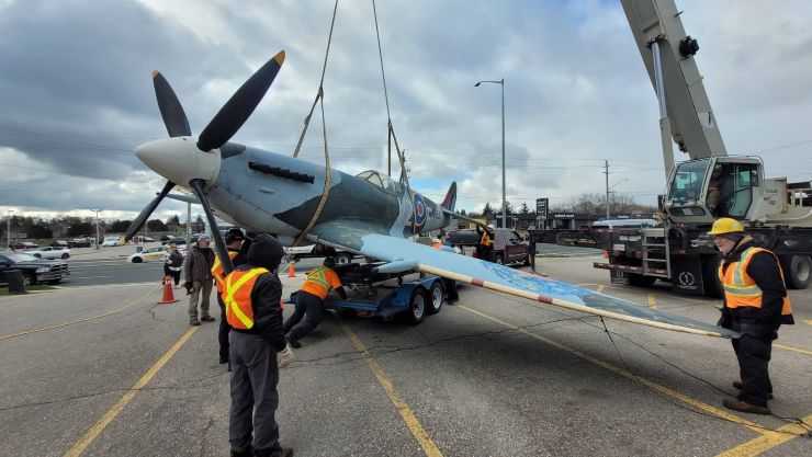 Replica Second World War Spitfire is lowered by crane onto the parking lot of K W Surplus.